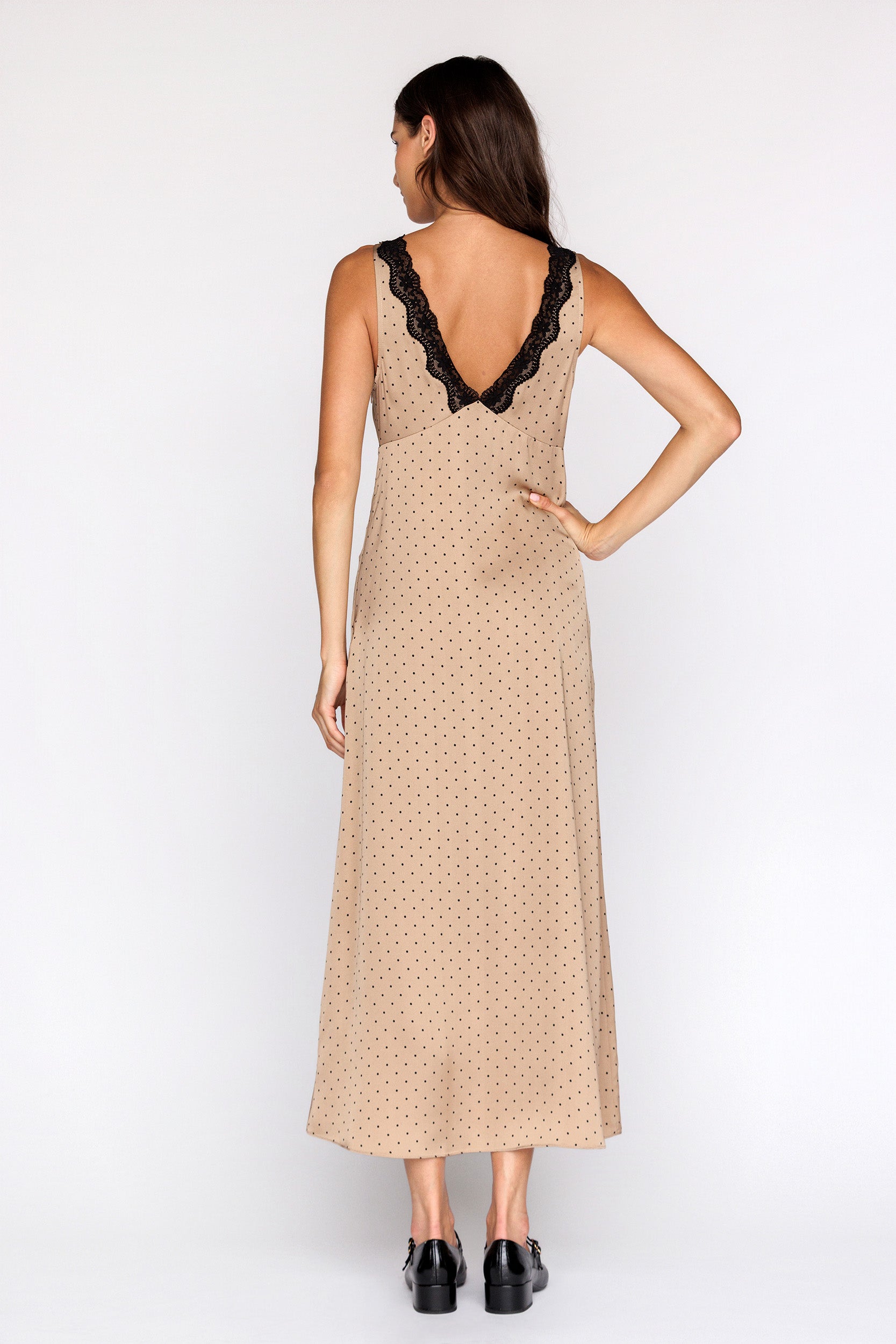Woman wearing a bronze with black polka dot dress with black lace details on a white background