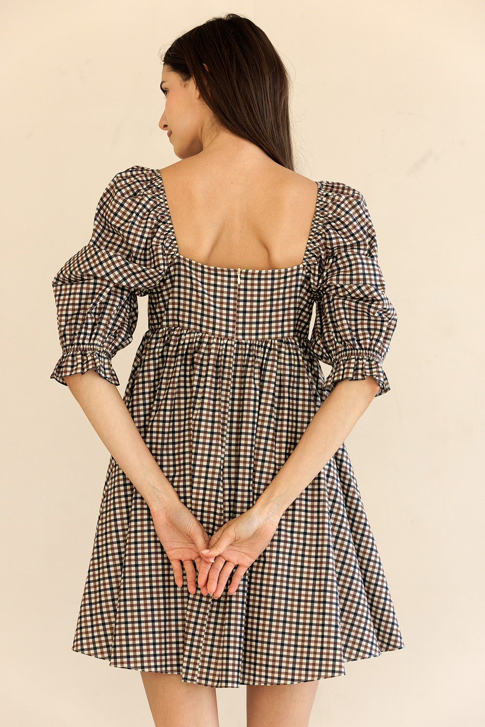 Woman wearing a brown checkered dress with puff sleeves on a beige background