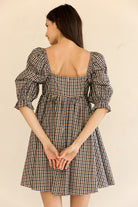 Woman wearing a brown checkered dress with puff sleeves on a beige background