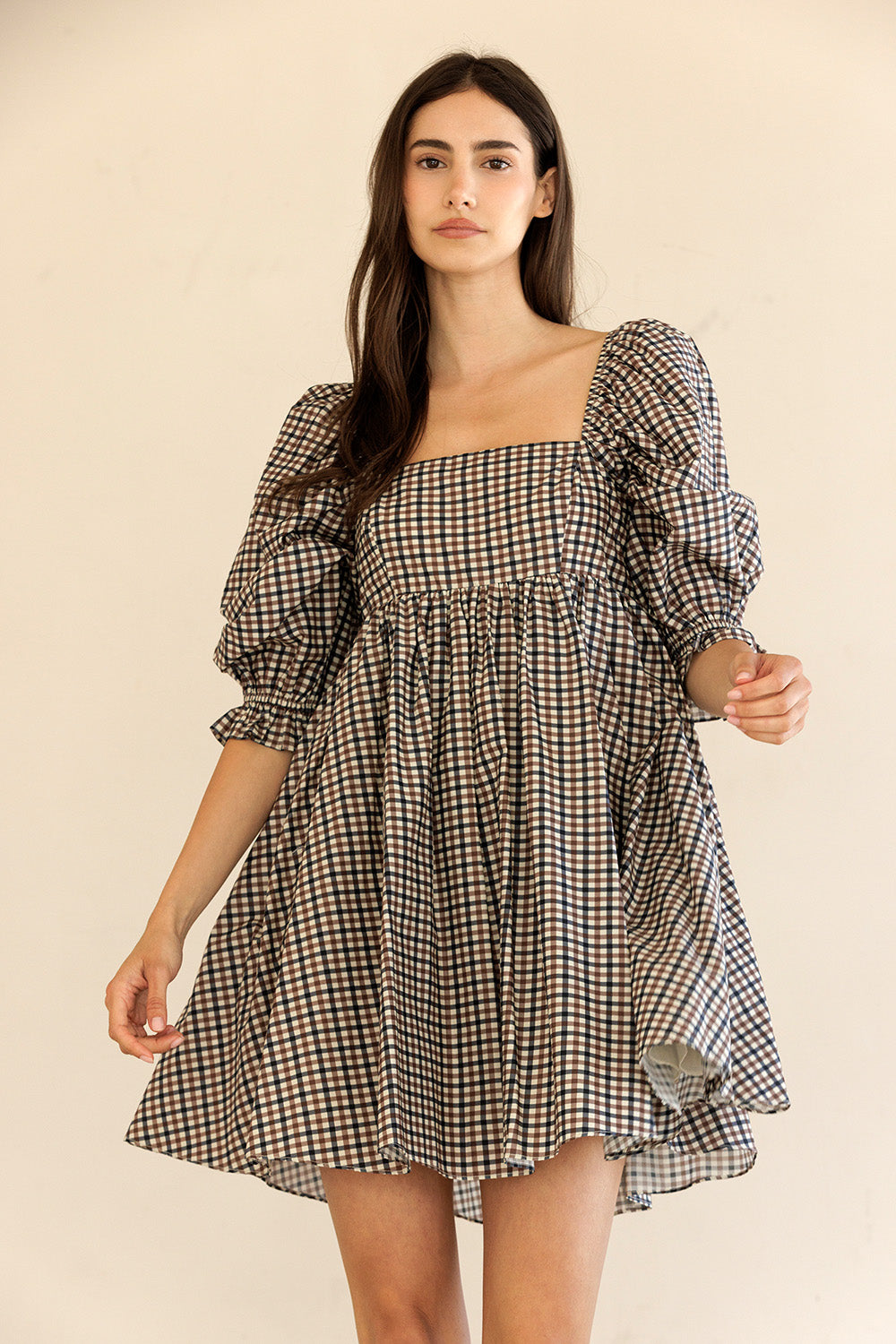 Woman wearing a checkered dress with puff sleeves against a beige background