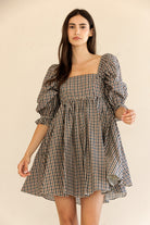 Woman wearing a checkered dress with puff sleeves against a beige background