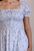 A person wearing a blue base dress with pink florals, a fully smocked bodice and puff sleeves.