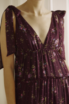 Close-up of a person wearing a plum base with an allover pink floral print dress with a deep v-neckline in a white background