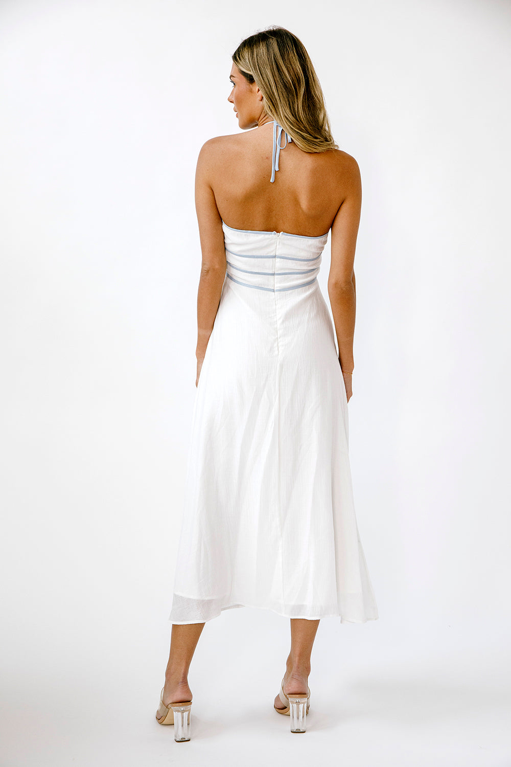 Back view of a woman wearing a white dress with blue accents on a white background