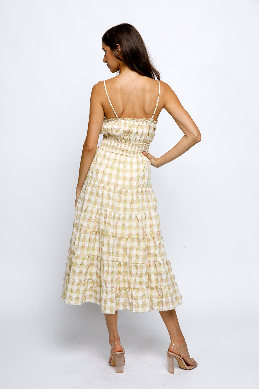 Back view of a woman wearing a yellow checkered dress on a white background