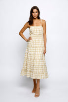 A woman wearing a yellow plaid midi dress with spaghetti straps and ruffled flowy bottom.
