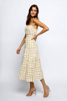 A woman wearing a yellow plaid midi dress with spaghetti straps, a high waist, and ruffled flowy bottom.