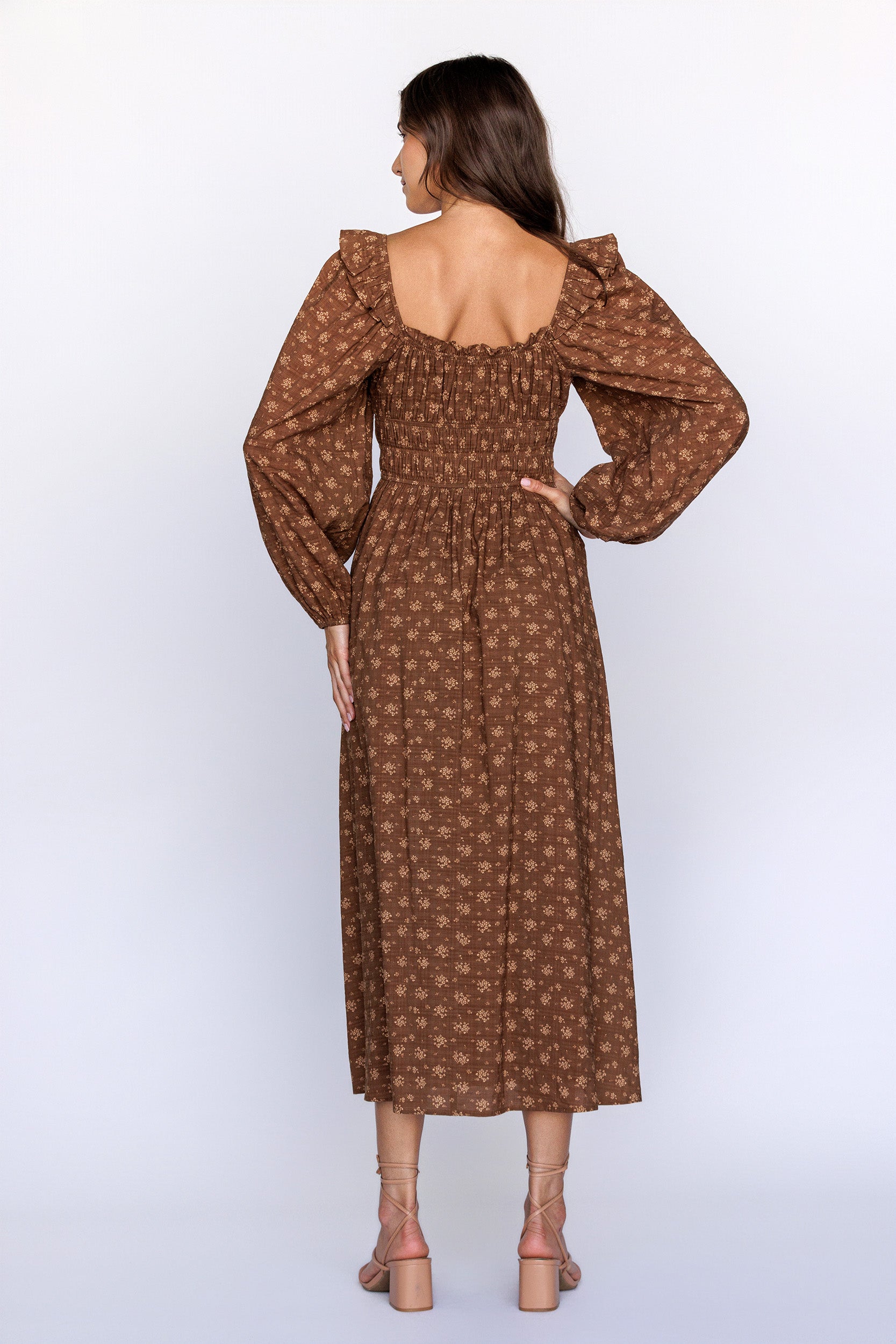 Back view of a woman wearing a brown patterned dress with long sleeves on a white background
