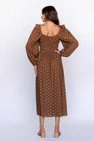 Back view of a woman wearing a brown patterned dress with long sleeves on a white background