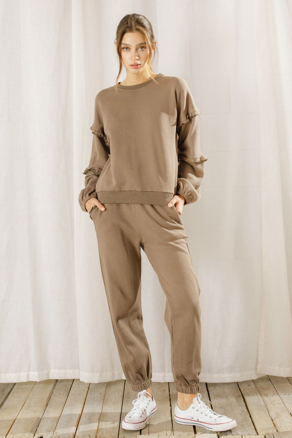 Woman wearing a brown sweatshirt and pants set with white sneakers against a neutral background