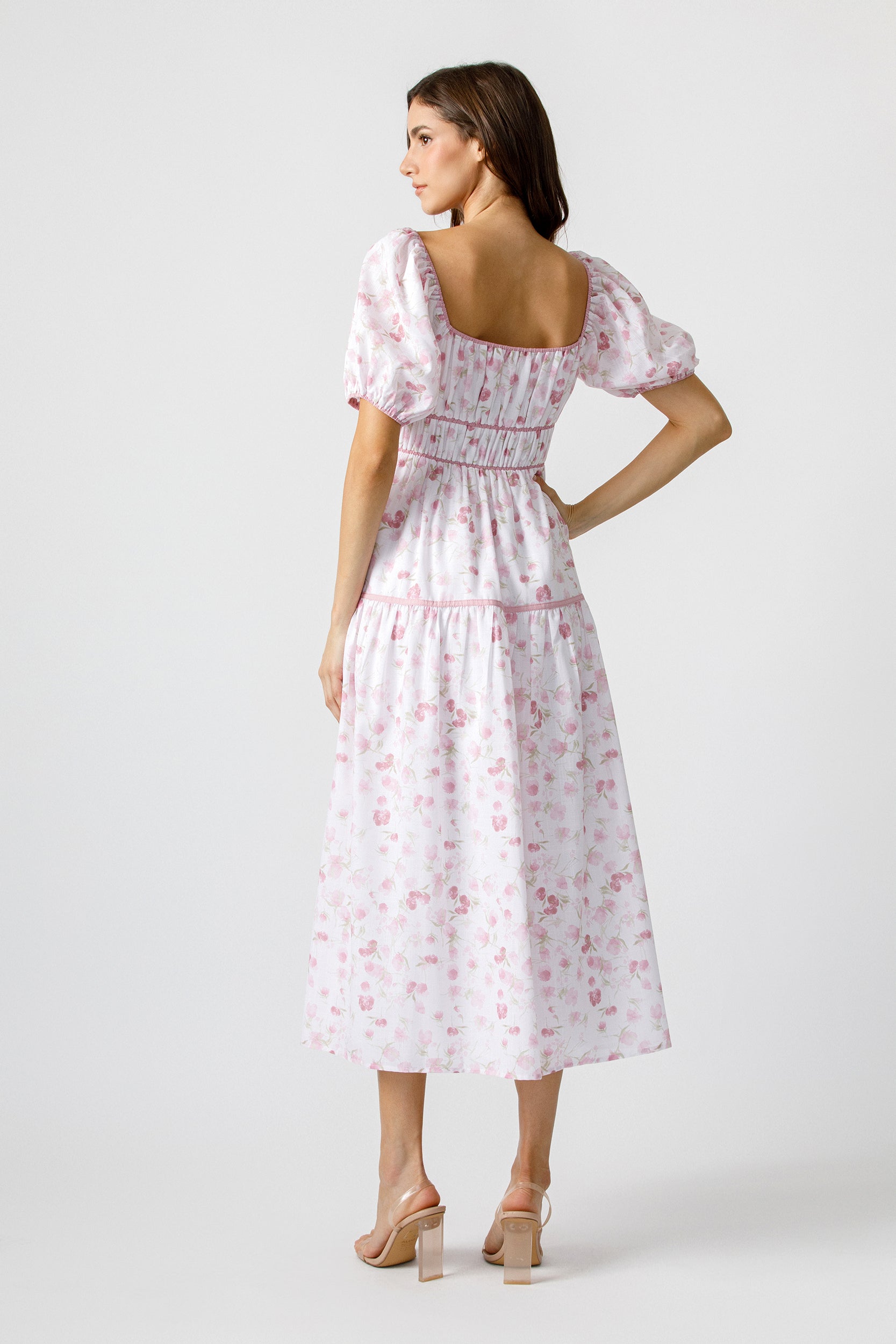 Back view of woman wearing a white dress with pink floral pattern on a white background