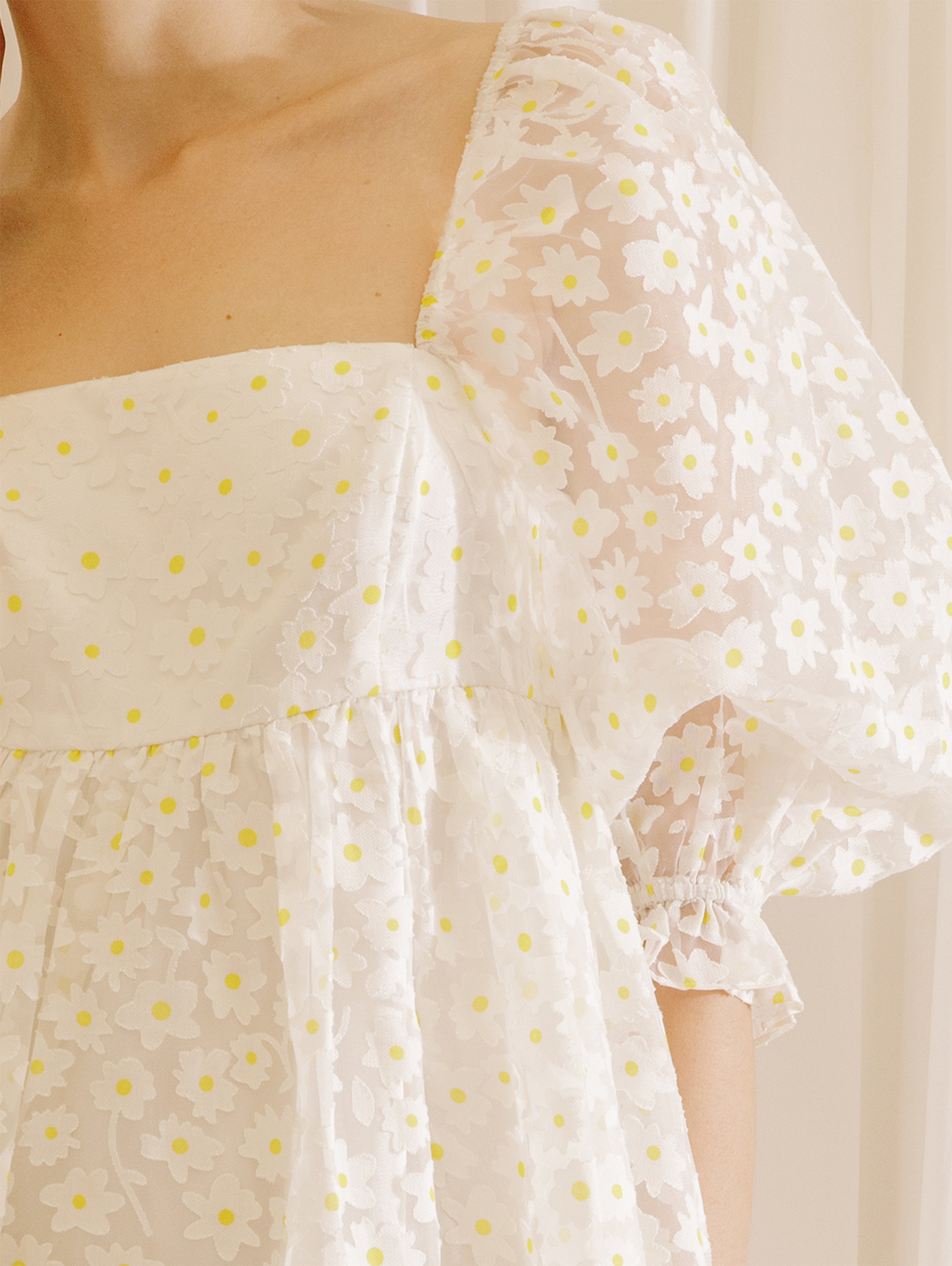 White dress with a sheer daisy-flocked fabric with yellow accents against a beige curtain background