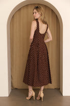 A woman viewed from behind wearing a brown polka dot midi dress standing in an archway and wearing beige high-heels.