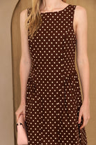 A person wearing a brown dress with ivory polka dots against a beige background