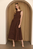 Woman wearing a brown polka dot midi dress standing in an archway with a beige curtain.