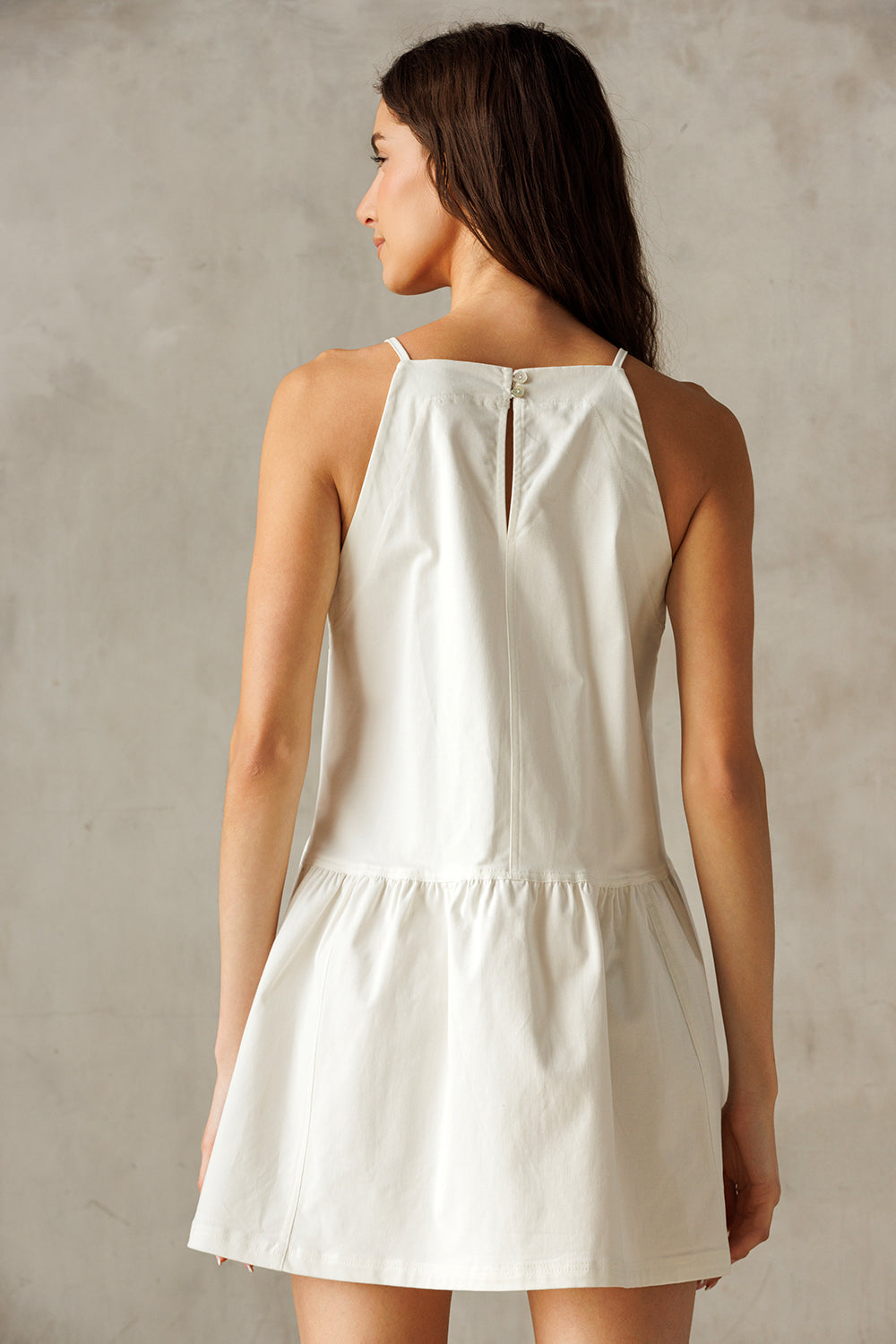 Back view of a woman wearing a flowy white dress against a neutral background