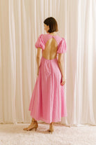 Woman wearing a pink plaid dress with open back against a white curtain background