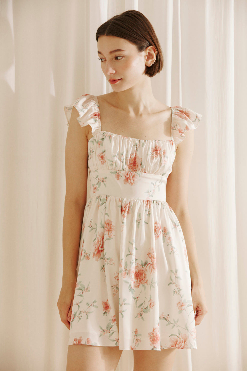 Woman wearing a cream floral mini dress against a plain background