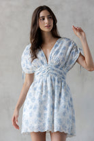 Woman wearing a blue floral dress with eyelet detailing throughout against a gray background