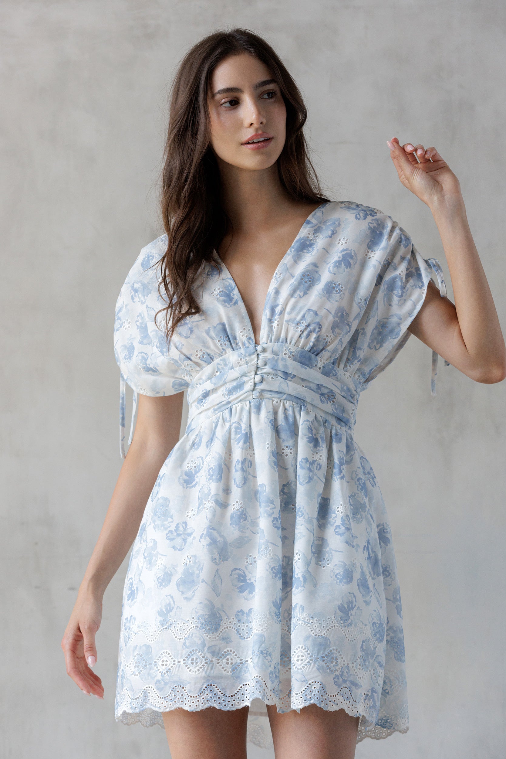 Woman wearing a blue floral dress with eyelet detailing throughout against a gray background