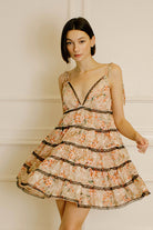 Woman wearing a peach floral dress with lace details against a neutral wall.
