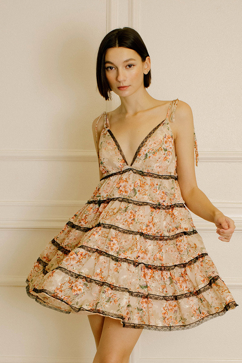 Woman wearing a peach floral dress with lace details against a neutral wall.