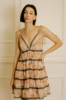 Woman wearing a peach floral dress with black lace details against a neutral wall.