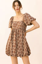Woman wearing a brown gingham with floral embroidery mini dress against a beige background