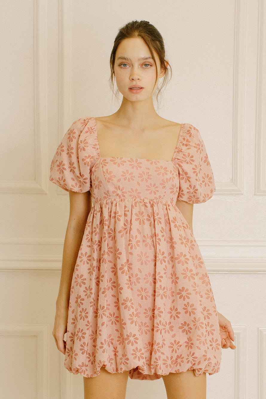 Woman wearing a pink gingham with floral embroidery mini dress against a neutral background