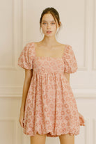 Woman wearing a pink gingham with floral embroidery mini dress against a neutral background