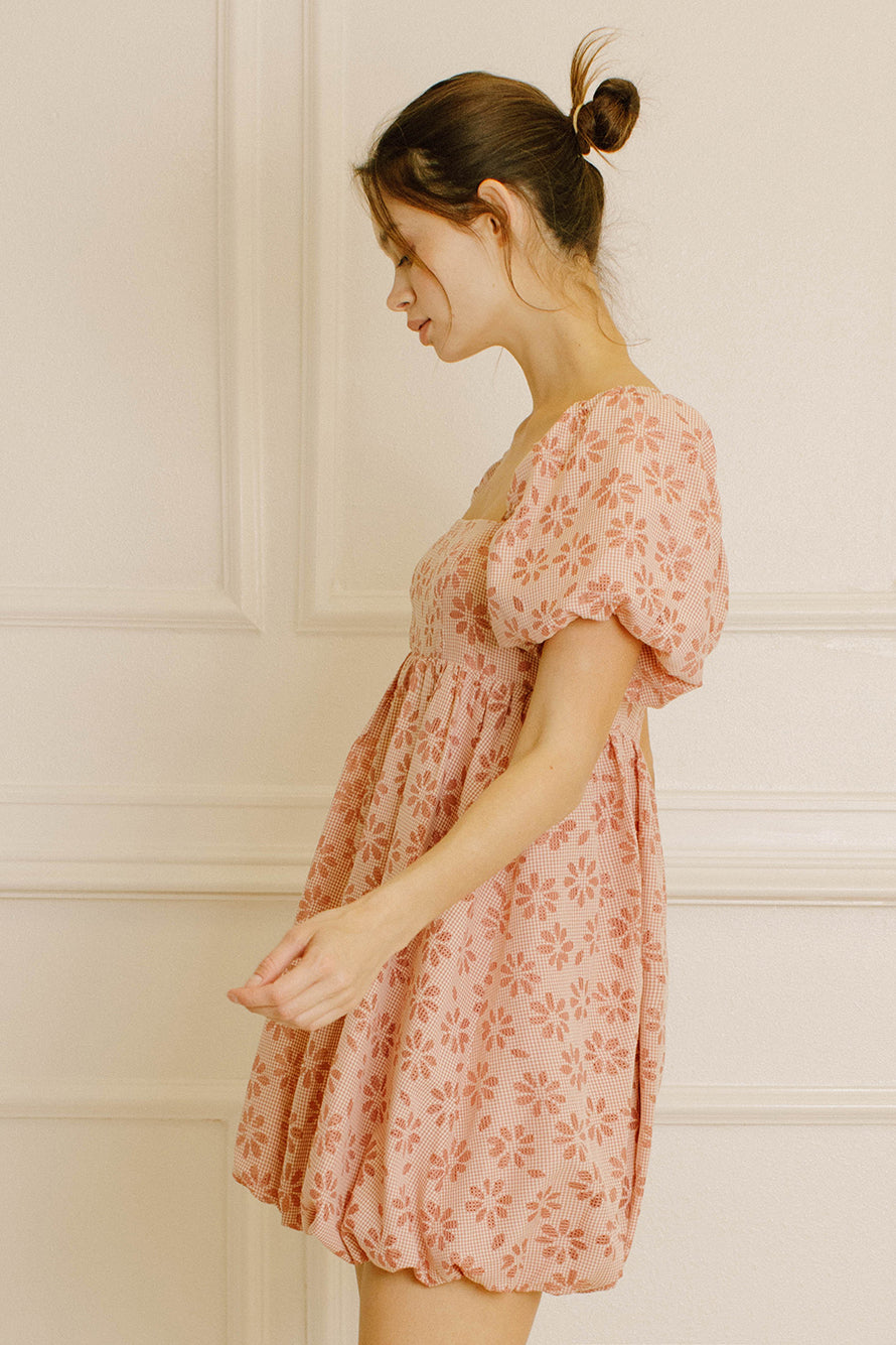 Side view of a woman wearing a pink gingham with floral embroidery mini dress against a neutral background