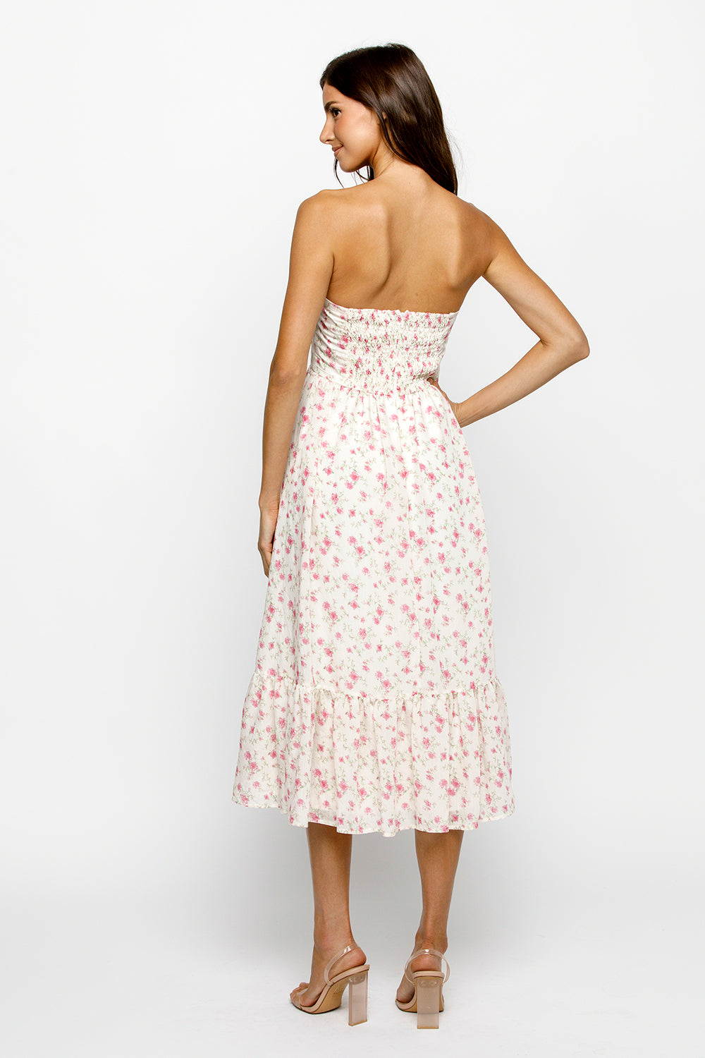 Back view of a woman wearing a strapless cream floral dress on a white background