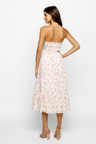 Back view of a woman wearing a strapless cream floral dress on a white background