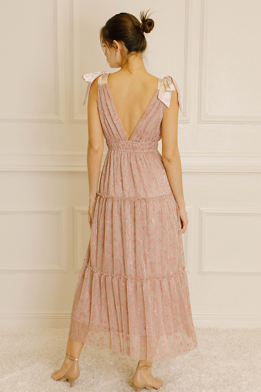 Back view of a woman wearing a pink metallic floral dress against a neutral wall.