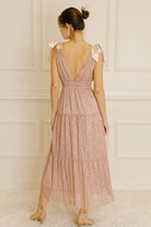 Back view of a woman wearing a pink metallic floral dress against a neutral wall.