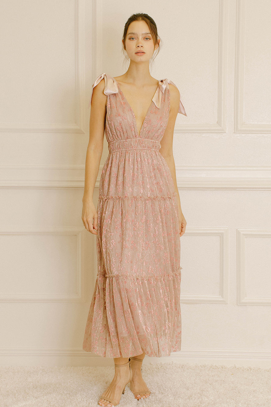 Woman wearing a pink metallic floral dress against a neutral wall.