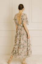 Woman wearing a beige floral dress with a backless design against a white paneled wall.
