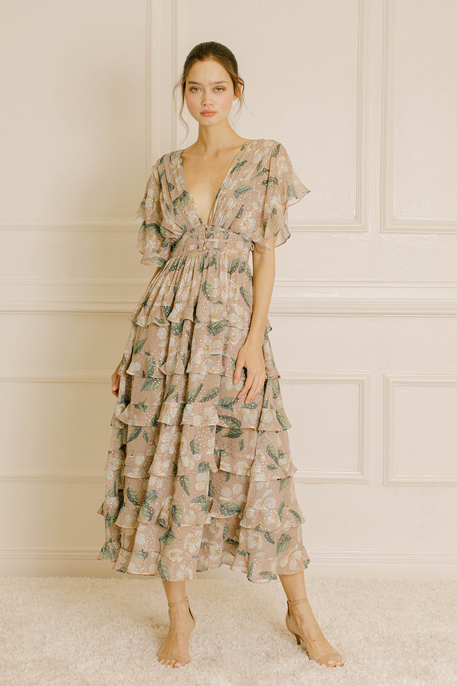 Woman wearing a beige and green floral dress in a room with white paneled walls.