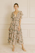Woman wearing a beige and green floral dress in a room with white paneled walls.