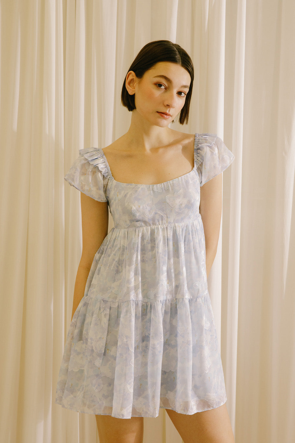 Woman wearing a light blue dress against a beige curtain background