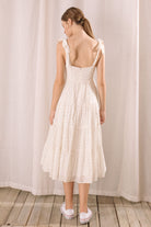 Back view of a woman wearing a white floral dress standing against a plain background