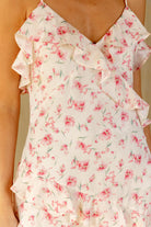 A close-up of a ruffled dress with a pink floral print on a cream background, worn by a model.
