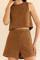 A model wearing a matching brown sleeveless crop top and high-waisted shorts set, photographed against a solid light beige background.