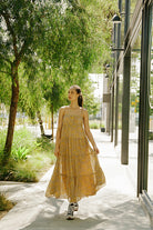Woman in a yellow dress walking outdoors near trees and a building.