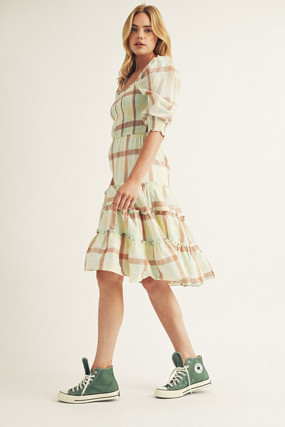 Woman wearing a plaid dress with green sneakers on a plain background
