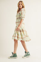 Woman wearing a plaid dress with green sneakers on a plain background