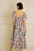 Back view of a woman wearing a pastel floral midi dress against a beige wall