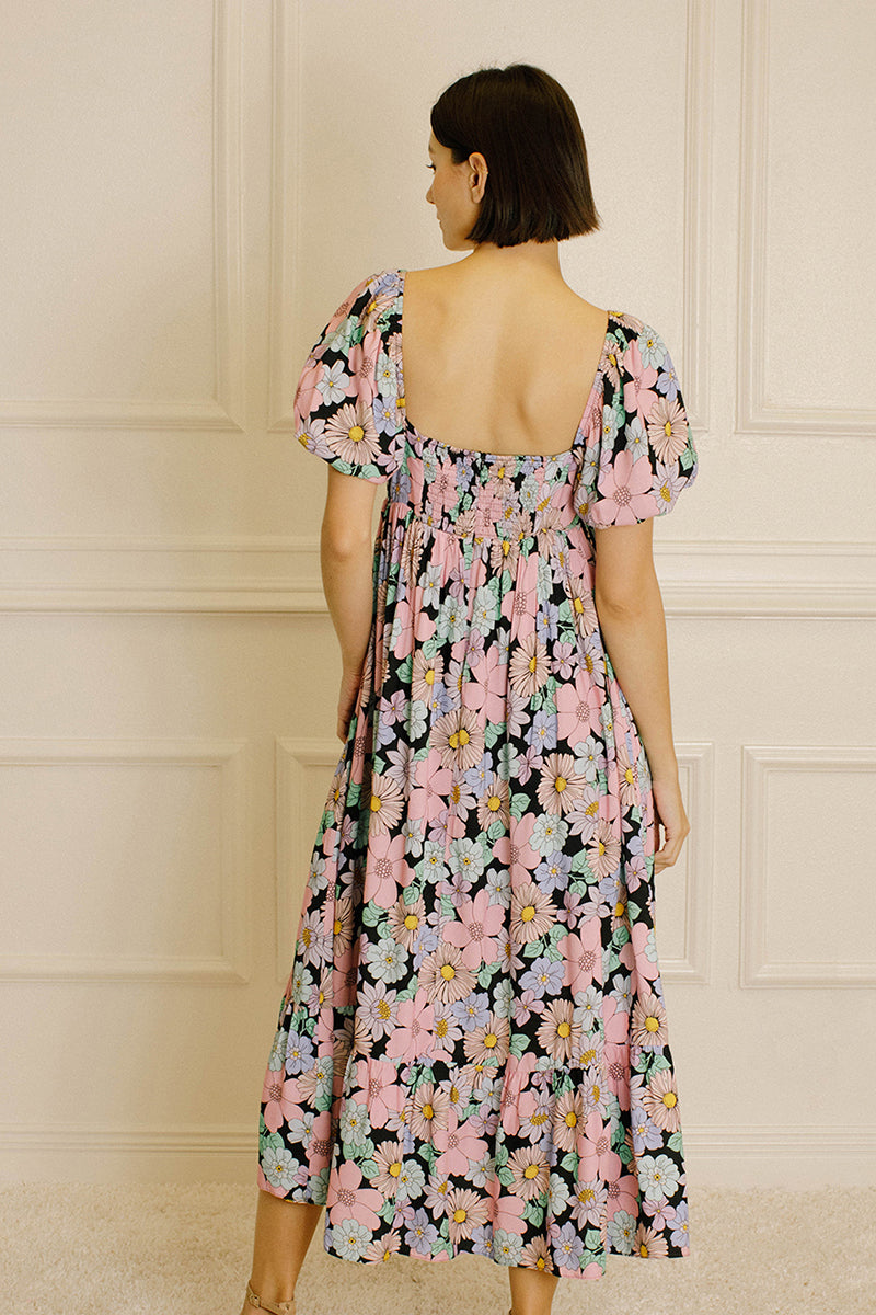 Back view of a woman wearing a pastel floral midi dress against a beige wall
