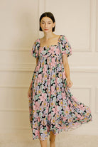 Woman wearing a pastel floral midi dress against a beige wall.