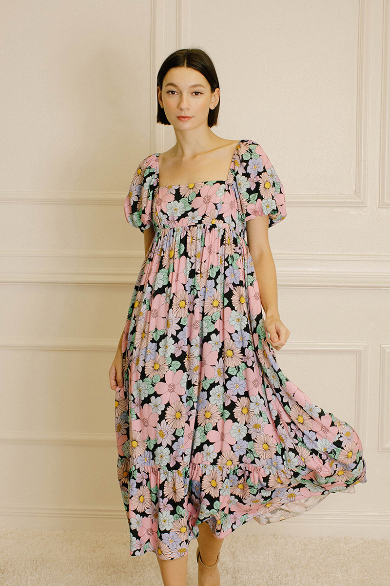 Woman wearing a pastel floral midi dress against a beige wall.